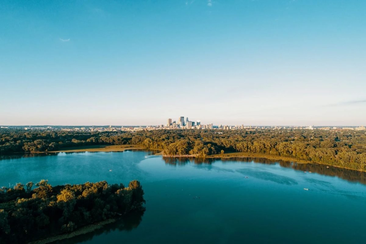 Un lago azul y parques verdes con el horizonte de Minneapolis a lo lejos