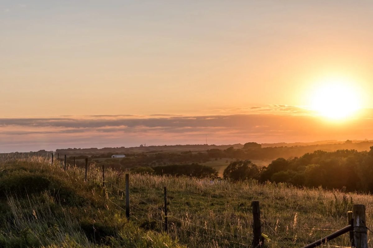 The sun rising over fields and a fence line in rural Nebraska