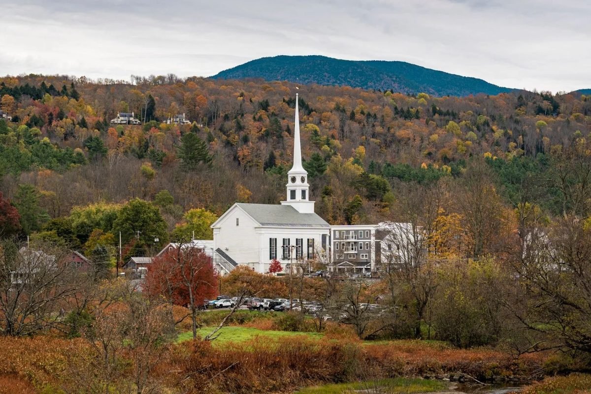 A white church steeple among fall color and green mountains in Stowe, Vermont